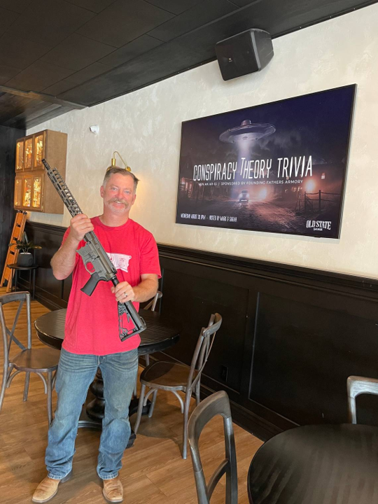 Old State Saloon owner Mark Fitzpatrick holds the AR-15 rifle that will be used as a prize. Old State Saloon/Facebook