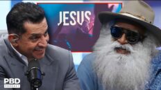 Two men on a PBD Podcast set: a suited host speaking into a microphone and a bearded guest wearing sunglasses and a hat, with a JESUS sign in the background.