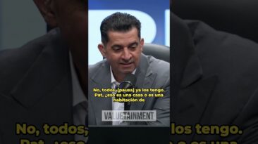 Man in a gray suit speaks into a microphone during a podcast, with yellow Spanish captions over the image About a house or room question.