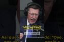 Man in a suit wearing headphones, speaking into a microphone during a live broadcast.