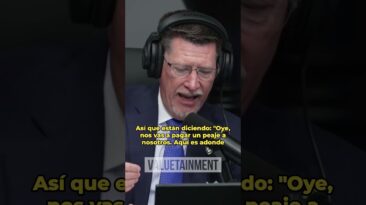 Man in a suit wearing headphones, speaking into a microphone during a live broadcast.